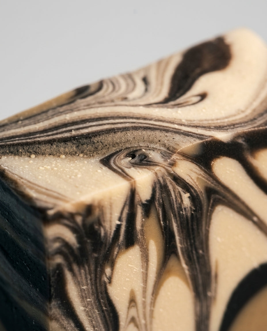 Detailansicht der kaltgerührten Kaffeeseife Coffee Kiss von PACATS COSMETIC MANUFACTURE. Das Nahaufnahme-Foto zeigt die feine Textur des Seifenleims, der auf einem schonenden Olivenöl-Kaffee-Ölauszug basiert. Die markante, dunkelbraun-beige Swirl-Marmorierung und die handwerkliche Qualität der Stückseife stehen im Fokus.