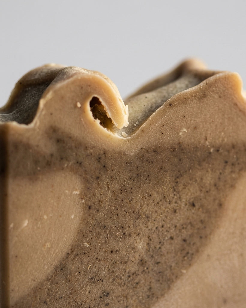 Detailansicht der rustikalen, geschwungenen Oberkante der Naturseife Olive-Vanilla von PACATS COSMETIC MANUFACTURE. Gut erkennbar ist die feine, matte Textur der Seife mit Mustern aus marokkanischer Lavaerde und Algenpulver in erdigen Beige- und Brauntönen.