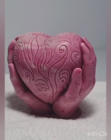 Handgemachte rosa Seife in Form eines großen Herzens, das von zwei Händen gehalten wird, verziert mit kunstvollen Schnörkeln, von PACATS Cosmetic Manufacture aus Zypern.